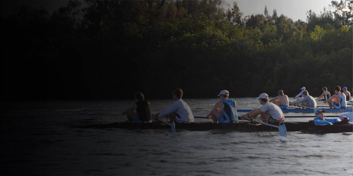 Rowers on a boat in a body of water with trees in the background